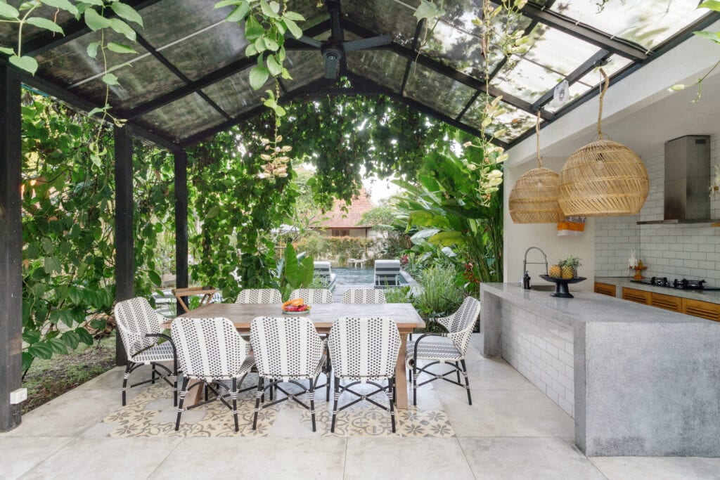Open keuken met lege eetkamertafel en stoelen buiten, tegen groene verse planten op achtergrond