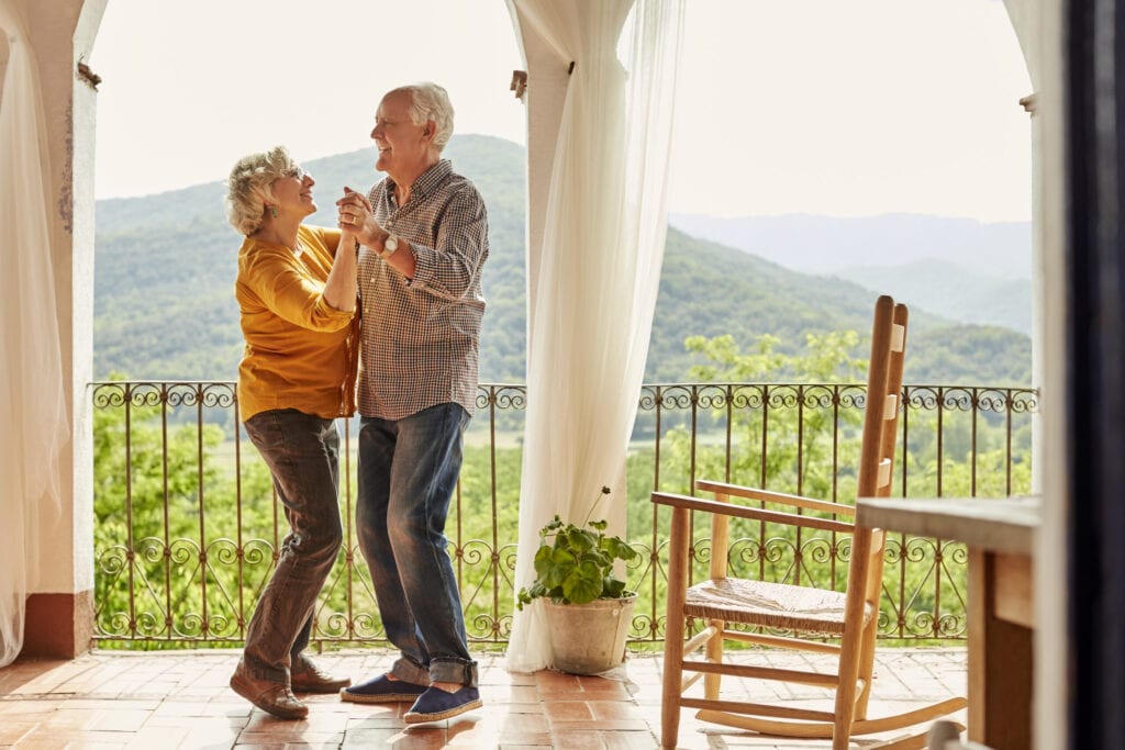 Liefdevol seniorenkoppel dansen op balkon. Gelukkige man en vrouw brengen samen vrije tijd door. Ze zijn thuis.