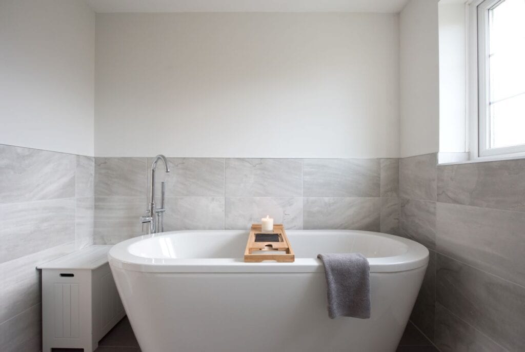 Badkamer met witte badrub en grijze tegel halverwege de muur, lambrisering stijl in badkamer