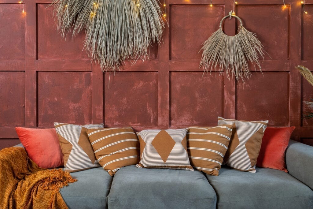 Elementen van gezellige kamer met boho stijl interieur, bank of bank en kussens, kussens in de buurt van decoratie plant compositie op oranje muur