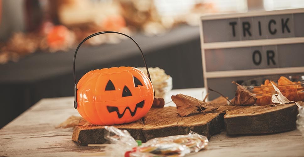 Een tafel versierd voor Halloween met een trick or treat teken en een jack-o-lantern mand voor snoep.
